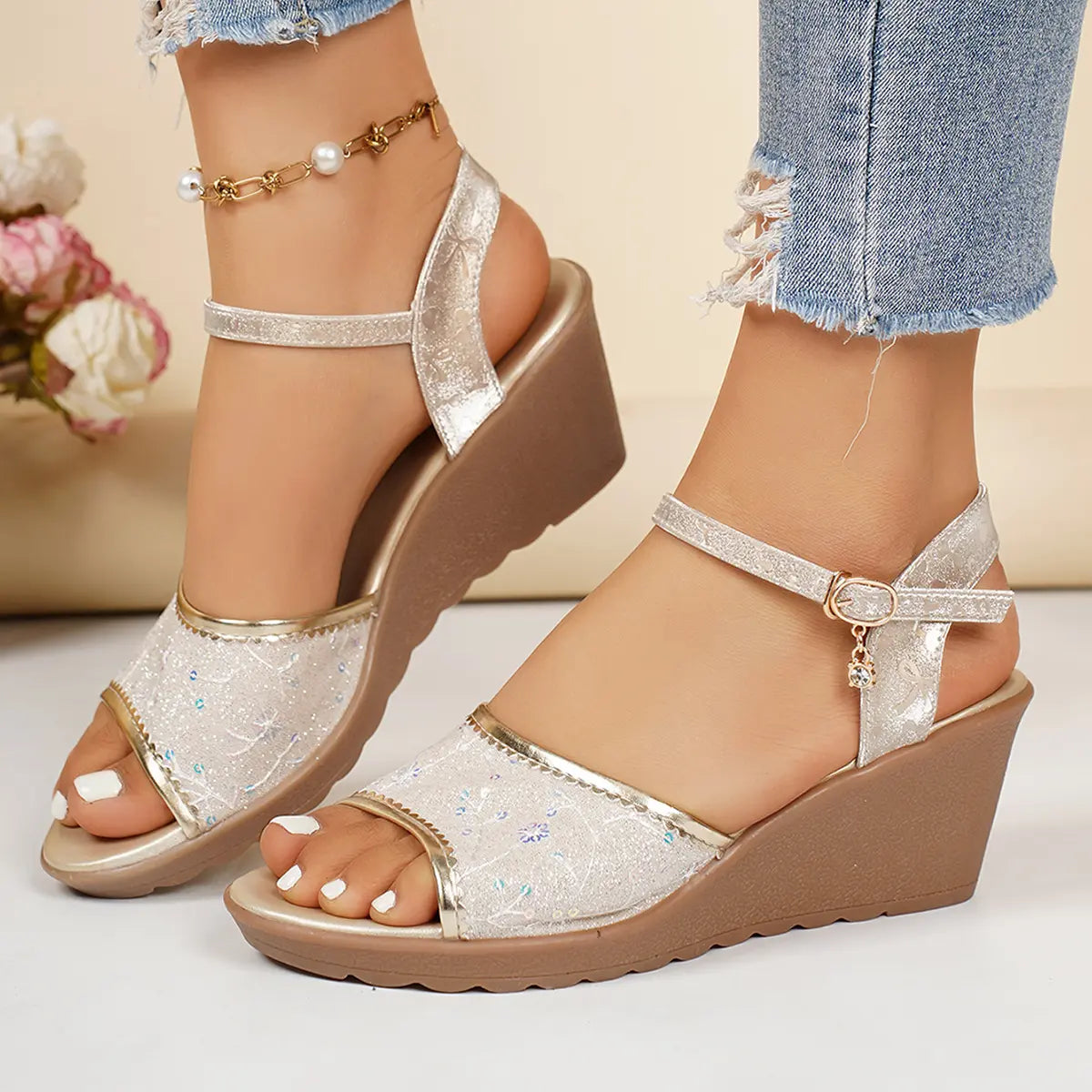 Women's pale gold embellished wedge sandals with delicate sequined floral embroidery and polished gold trim, shown on feet with rolled denim jeans and an ankle strap.