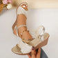 Close-up of gold embellished wedge sandals with peep toe and ankle strap, styled on a woman's foot with distressed jeans in a studio setting.