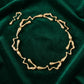 Radiant gold liquid metal choker necklace with abstract wavy links and a coordinating drop earring, displayed on plush emerald velvet.
