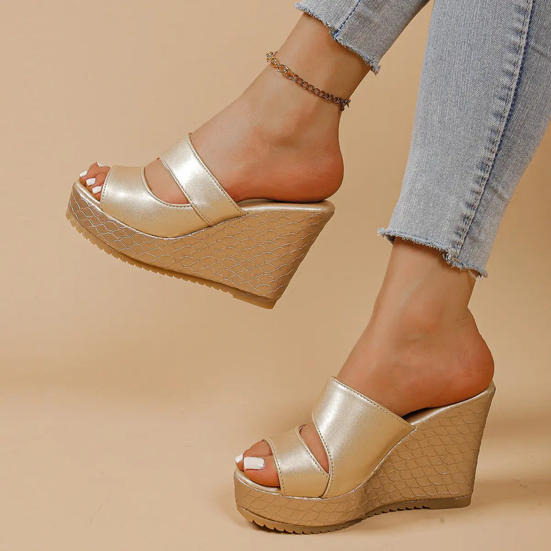 Gold metallic peep-toe platform wedge sandals with crossed straps and textured snake-effect wedge heel, worn by a woman with blue jeans and an anklet.