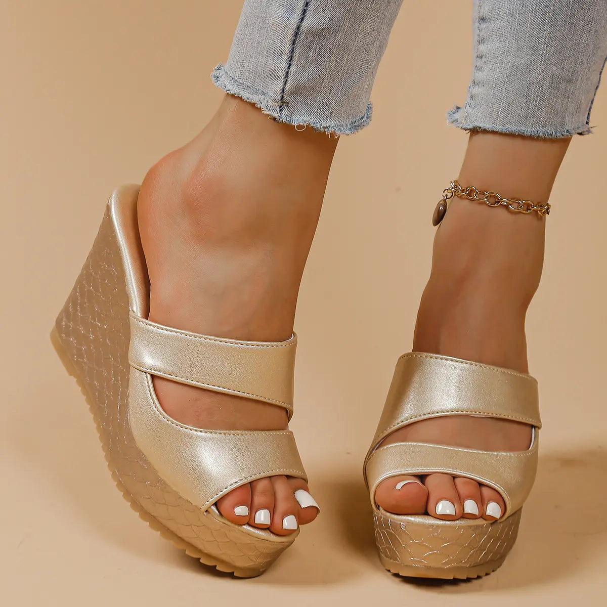 Gold peep-toe platform wedge sandals with intersecting straps and a textured snake-effect wedge heel, worn with distressed denim jeans.