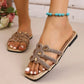 Close-up of elegant gold flat slide sandals adorned with floral rhinestone embellishments on a woman's foot with white nail polish and a turquoise anklet.