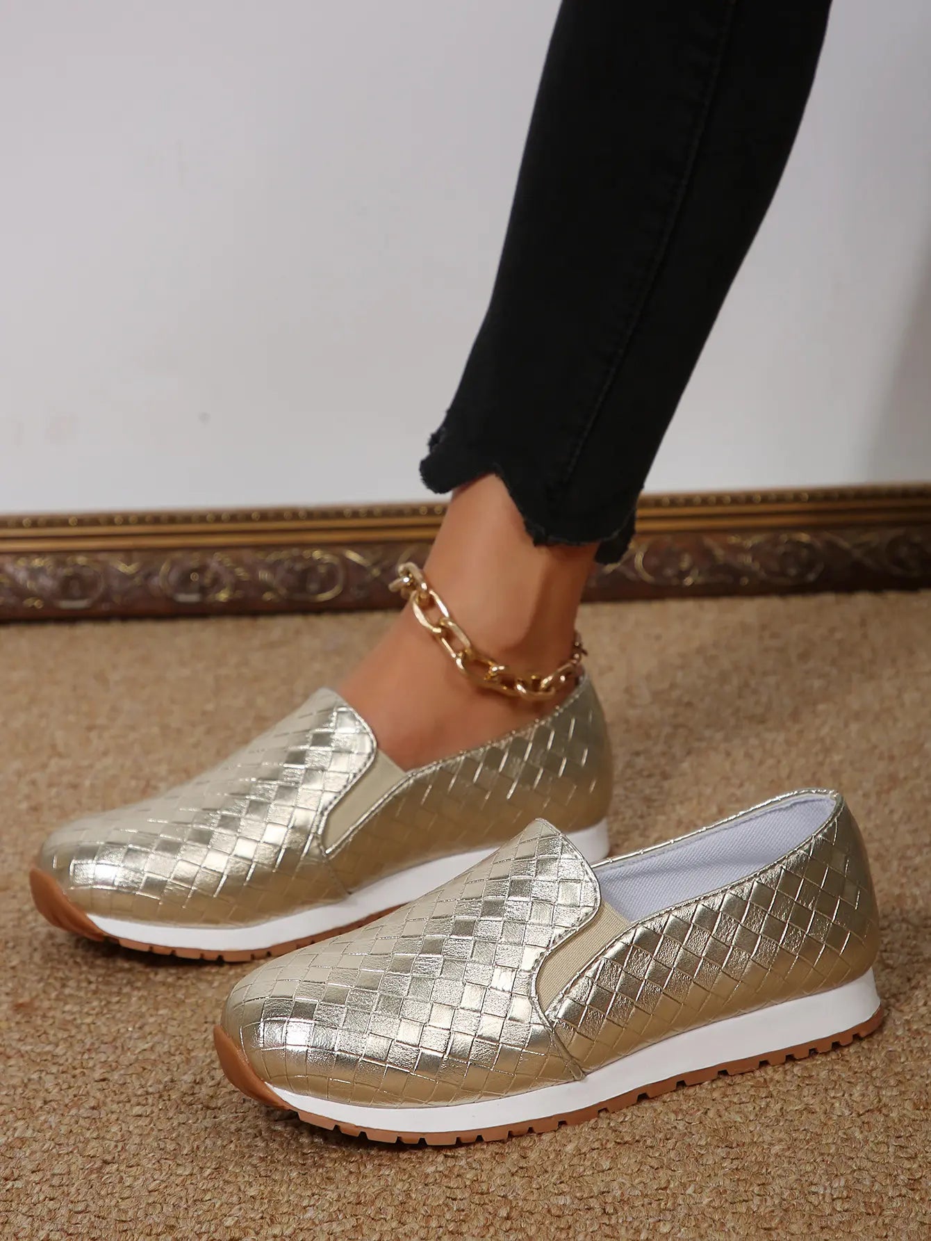 Women's metallic gold woven slip-on loafers worn with black cropped jeans and a gold ankle chain, showcasing the woven texture and comfortable design.