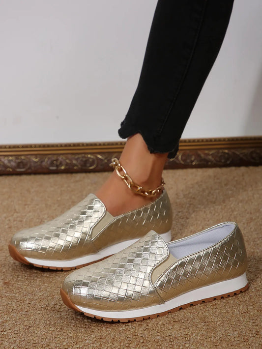 Women's metallic gold woven slip-on loafers worn with black cropped jeans and a gold ankle chain, showcasing the woven texture and comfortable design.