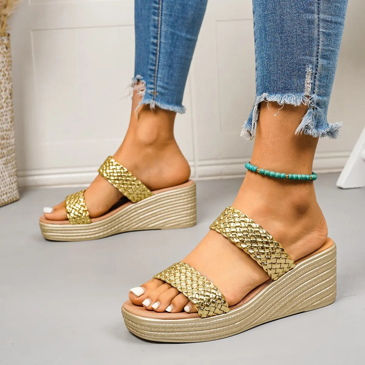 Women's gold woven double strap platform wedge sandals shown on foot with ripped jeans, featuring a comfortable slip-on design and a sculpted champagne gold wedge heel.