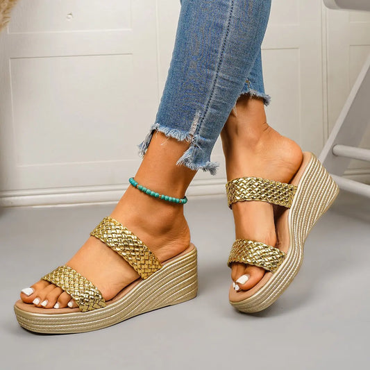 Close-up of a woman wearing gold woven strap platform wedge sandals with a champagne gold sole and tan footbed, paired with distressed blue jeans.
