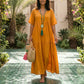 Woman wears a flowing Kivori Golden Amber tiered maxi dress, featuring a deep V-neck, short sleeves, and crinkled gauze texture, walking outdoors.