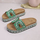 Green embellished platform slide sandals featuring intricate bead and rhinestone detailing on the strap, U-shaped cutouts, a natural cork footbed, and a decorative woven midsole. These open-toe slides offer a bohemian and chic summer style.