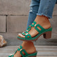Green heeled platform slide sandals with geometric gold-tone hardware and white contrast stitching, worn with distressed denim jeans.
