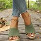 Woman's feet wearing green knitted espadrille wedge sandals with open toe and platform sole, styled with ripped denim jeans on a rustic wooden boardwalk.