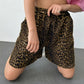Woman in high-rise leopard print shorts and a pink crop top kneeling, showcasing the relaxed wide-leg fit and bohemian street style.