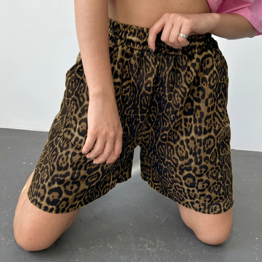Woman in high-rise leopard print shorts and a pink crop top kneeling, showcasing the relaxed wide-leg fit and bohemian street style.