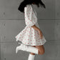 A woman in a white cotton-linen blend midi dress with a red heart print, featuring voluminous puff sleeves and a flared A-line skirt, styled with white boots.