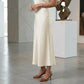 Model wearing a high-waisted Pearl White satin midi skirt, showcasing its luminous A-line drape and elegant mid-calf length in a sophisticated gallery setting.