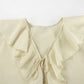Close-up of an ivory cream ruffle blouse neckline, showcasing tiered ruffles, a V-neck with adjustable tie closure, and a size M label on the inner collar.
