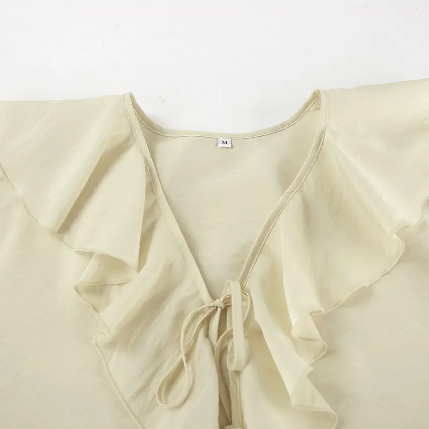 Close-up of an ivory cream ruffle blouse neckline, showcasing tiered ruffles, a V-neck with adjustable tie closure, and a size M label on the inner collar.