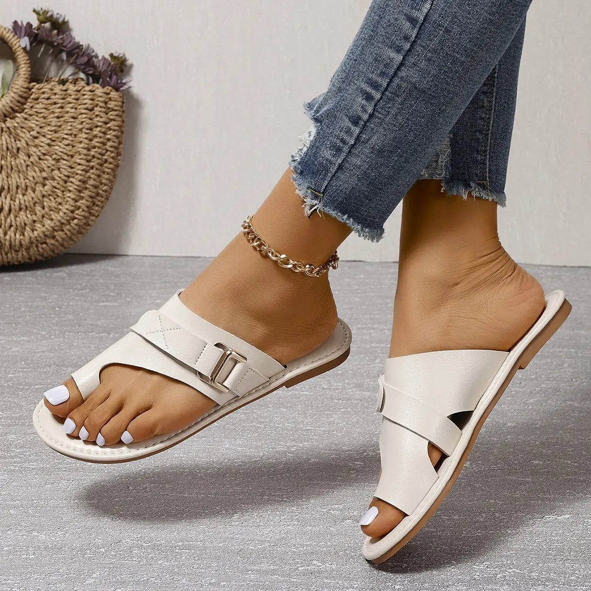 Elegant ivory leather flat sandals with crisscross straps and a toe-thong design, worn with distressed jeans and gold anklet for a chic summer look.