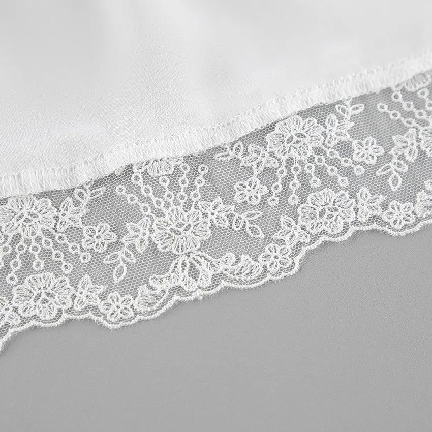 Close-up view of ivory satin fabric with delicate white floral lace trim along the hem, showcasing intricate embroidery and scalloped edging.