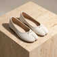 Lurran ivory white split-toe ballet flats in matte vegan leather with a delicate toe cleft bow, displayed three-quarter view on a light studio surface.