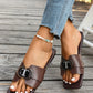 Chocolate brown Izoak square-toe flat slide sandals with a decorative crystal-inlaid 'T' buckle, worn by a woman with distressed denim jeans.