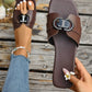 Chocolate brown Izoak square-toe flat slide sandals with a decorative embellished buckle featuring crystal accents, worn on a woman's foot with denim jeans.