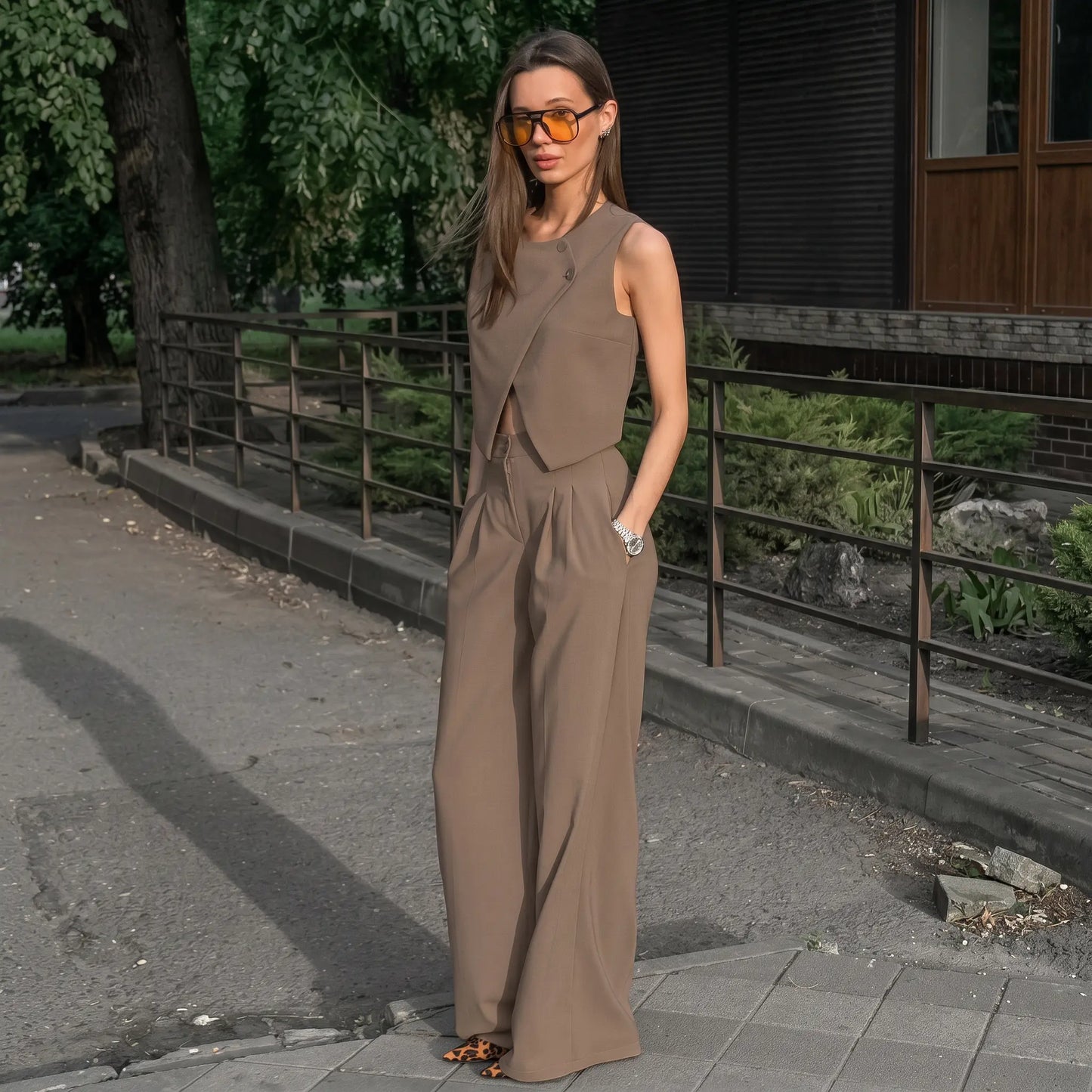 Chic beige Jovik women's vest and wide-leg trouser set worn by a model outdoors, showcasing the asymmetrical crossover vest and high-waisted pleated trousers.