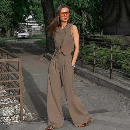 A chic beige asymmetrical crossover vest and high-waisted pleated wide-leg trouser set worn by a woman outdoors, showcasing its elegant drape and sophisticated silhouette.