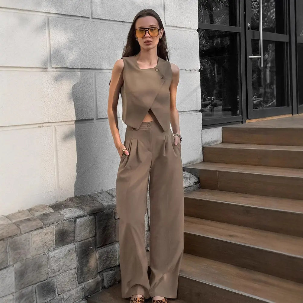 Woman modeling a chic beige sleeveless vest with an asymmetrical crossover front and high-waisted wide-leg trousers in an outdoor setting.