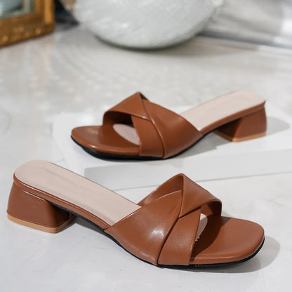 A pair of caramel brown Kaelan square-toe slide sandals with a chic twisted strap detail and a stable 4cm block heel, shown from a three-quarter front view on a studio background.