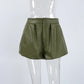 Kaelan high-waist olive green faux leather shorts with balloon silhouette and structured front pleats, presented on a mannequin from a front view.