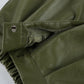 Close-up view of olive green high-waist faux leather shorts, showcasing the button closure, concealed zipper fly, sharp front pleats, and smooth material texture.