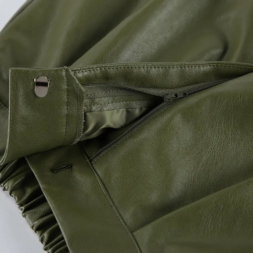 Close-up view of olive green high-waist faux leather shorts, showcasing the button closure, concealed zipper fly, sharp front pleats, and smooth material texture.