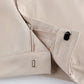 Close-up of neutral beige Kaelen wide-leg trousers showcasing the concealed side zipper, button closure, and subtle metallic accent on the hem.