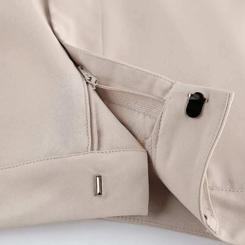 Close-up of neutral beige Kaelen wide-leg trousers showcasing the concealed side zipper, button closure, and subtle metallic accent on the hem.