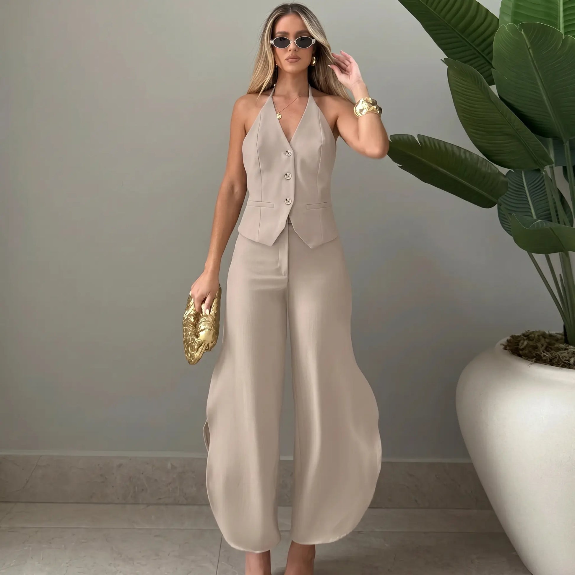 Model wearing a chic beige V-neck halter vest and flowing wide-leg palazzo trousers, styled with sunglasses and a clutch. This sophisticated two-piece ensemble offers a polished look.