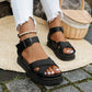 Women's black Kaelen chunky platform sandals with criss-cross straps and a buckle ankle strap, styled with ripped white jeans in a natural outdoor setting.