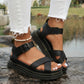 Kaelen black chunky sole platform sandals with criss-cross vamp straps and buckle ankle closure, styled with ripped white jeans on natural rocks.