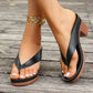 Elegant black Kaelen heeled slides with a thong toe post and substantial platform, shown on feet with white nail polish, resting on a weathered wooden deck.