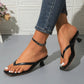 A pair of Kaelen heeled thong sandals in classic black, worn by a model showcasing the square toe and sculpted block heel against a textured white tiled background.