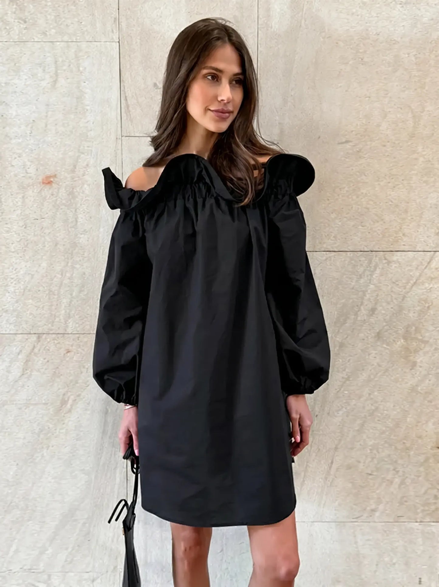 Model wearing a black Kaelen off-shoulder cotton mini dress with voluminous balloon sleeves and a gathered ruffle neckline.