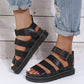 Black Kaelen platform gladiator sandals with chunky sole and black buckle strap, shown on a woman's feet with rolled jeans.