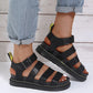 Black Kaelen platform gladiator sandals shown on a person's feet, featuring a chunky 3cm sole with yellow stitching detail and a black buckle ankle strap.