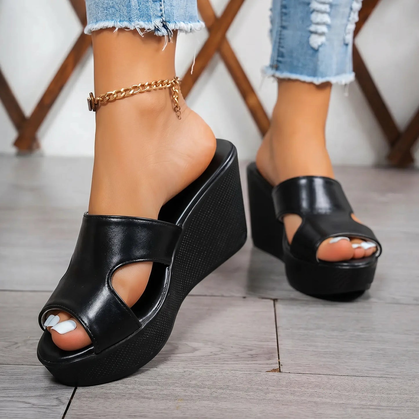 Black Kaelen wedge platform mules with a peep-toe front and single geometric cutout strap, styled with ripped denim jeans and a gold anklet.