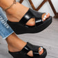 Black Kaelen wedge platform mules with a glossy patent finish, featuring a chic peep-toe and single vamp strap. Styled on a model's feet with ripped denim jeans.