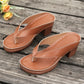 Brown PU leather heeled slides with thong strap and platform sole, shown at a three-quarter angle on a rustic wooden surface with yellow roses.