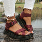 Deep wine red Kaelen platform sandals featuring criss-cross straps and a chunky lugged sole, worn by a model with ripped white jeans on natural rock formations.
