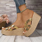 Kaelen gold metallic wedge espadrille sandals featuring criss-cross straps and a thick platform sole, shown from a three-quarter angle on a wooden floor with a brick wall backdrop.