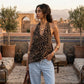 Model wearing a Kaelen leopard print halter neck top with a deep V-neckline, styled with light blue jeans on an outdoor rooftop terrace.