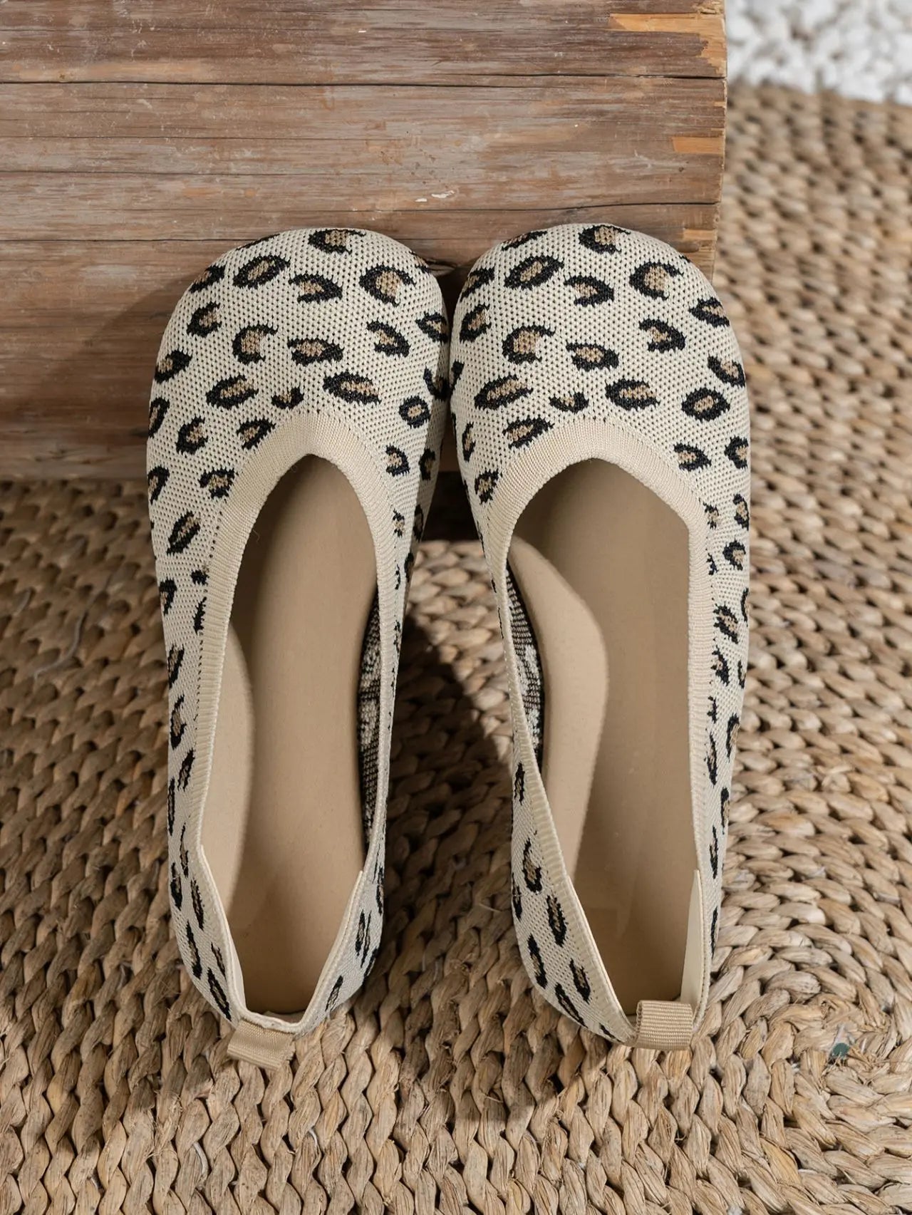 A pair of women's Kaelen knit ballet flats featuring a classic leopard print in black and brown on a creamy off-white base. These slip-on shoes have a round toe and flat sole, presented on a textured woven mat.