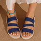 Model's feet wearing Kaelen navy blue flat sandals with woven elastic straps and a braided sole trim, accented with a turquoise beaded anklet.